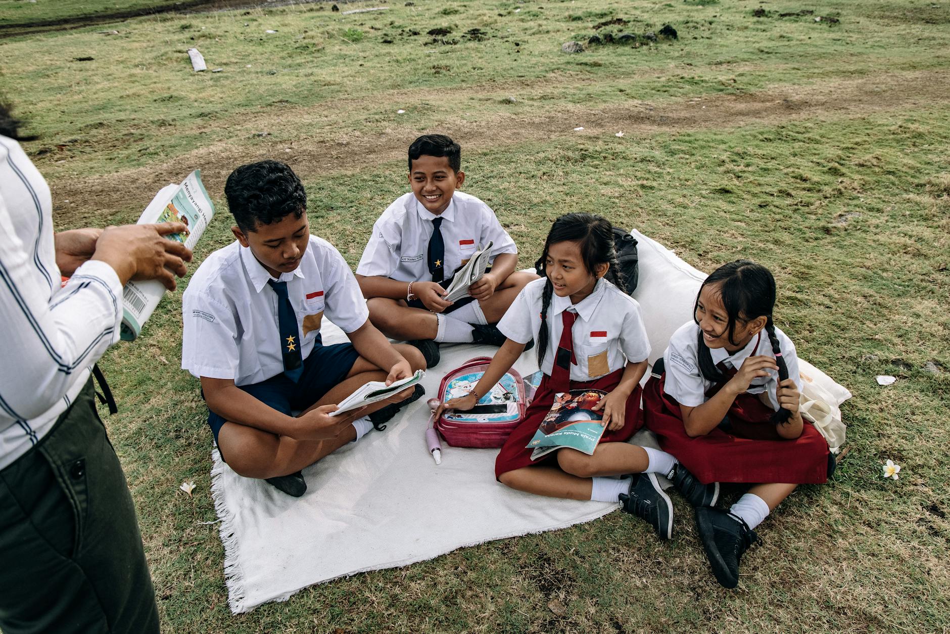 Indonezyjscy uczniowie w mundurkach czytają razem na trawie
