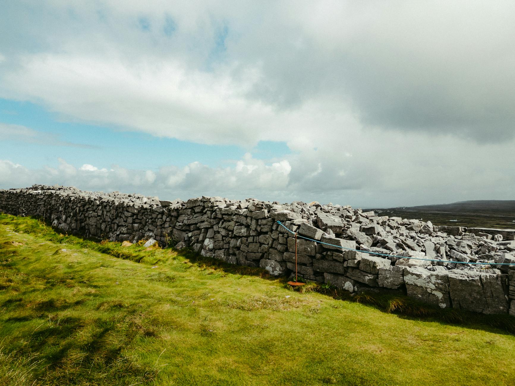 Jak czytać irlandzkie krajobrazy: mury z kamieni, torfowiska, wrzosowiska i ich historie Kamienny mur w hrabstwie Clare w Irlandii pod pochmurnym niebem