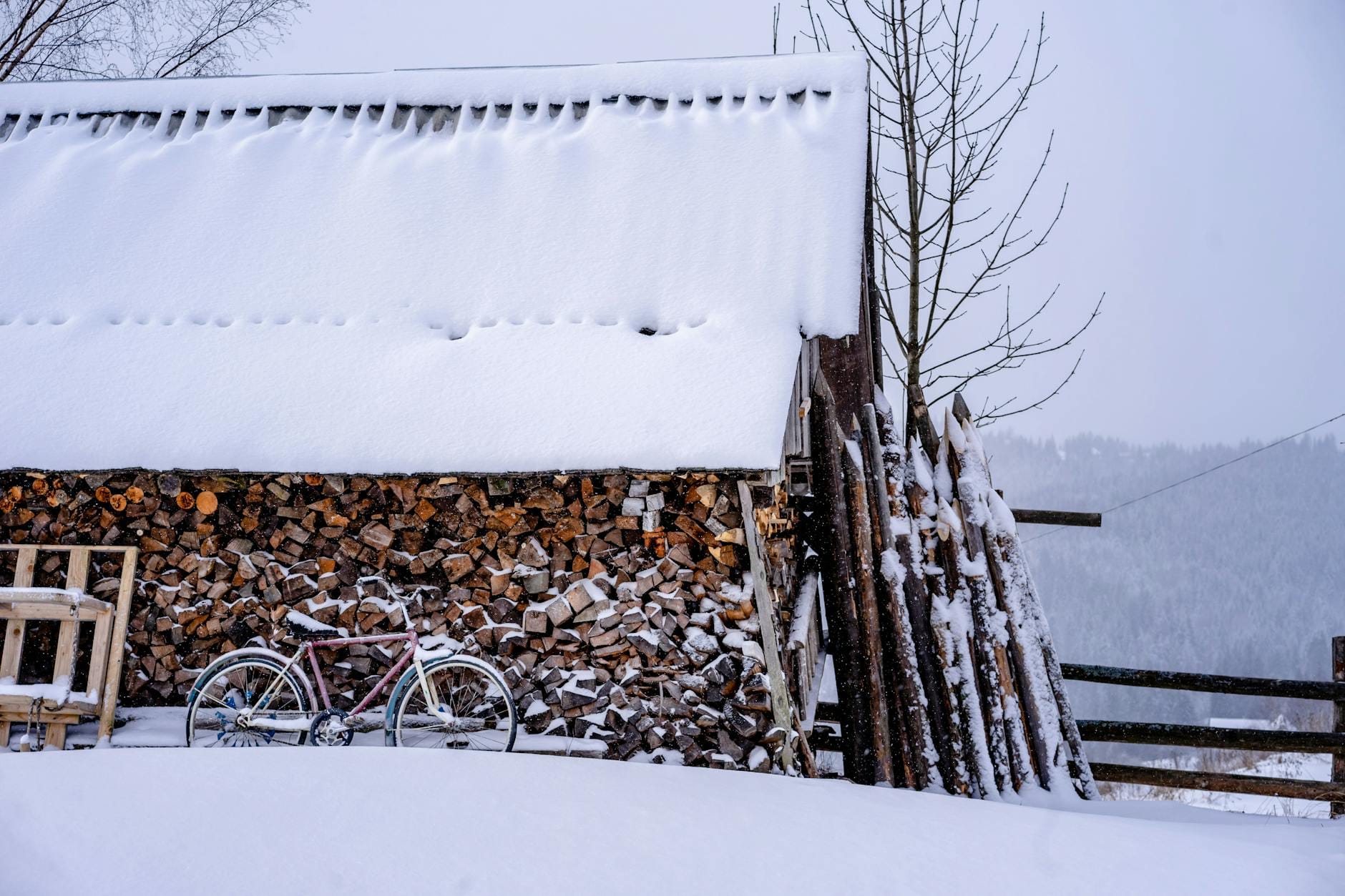 Zasypany śniegiem drewniany składzik z drewnem i rowerem w Bukowelu